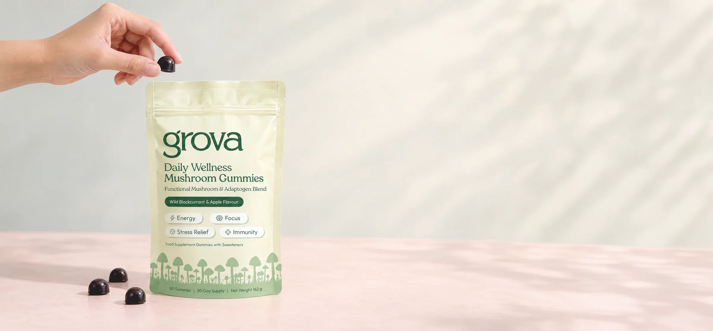 A hand holding a gummy above a pouch of Grova Daily Wellness Mushroom Gummies