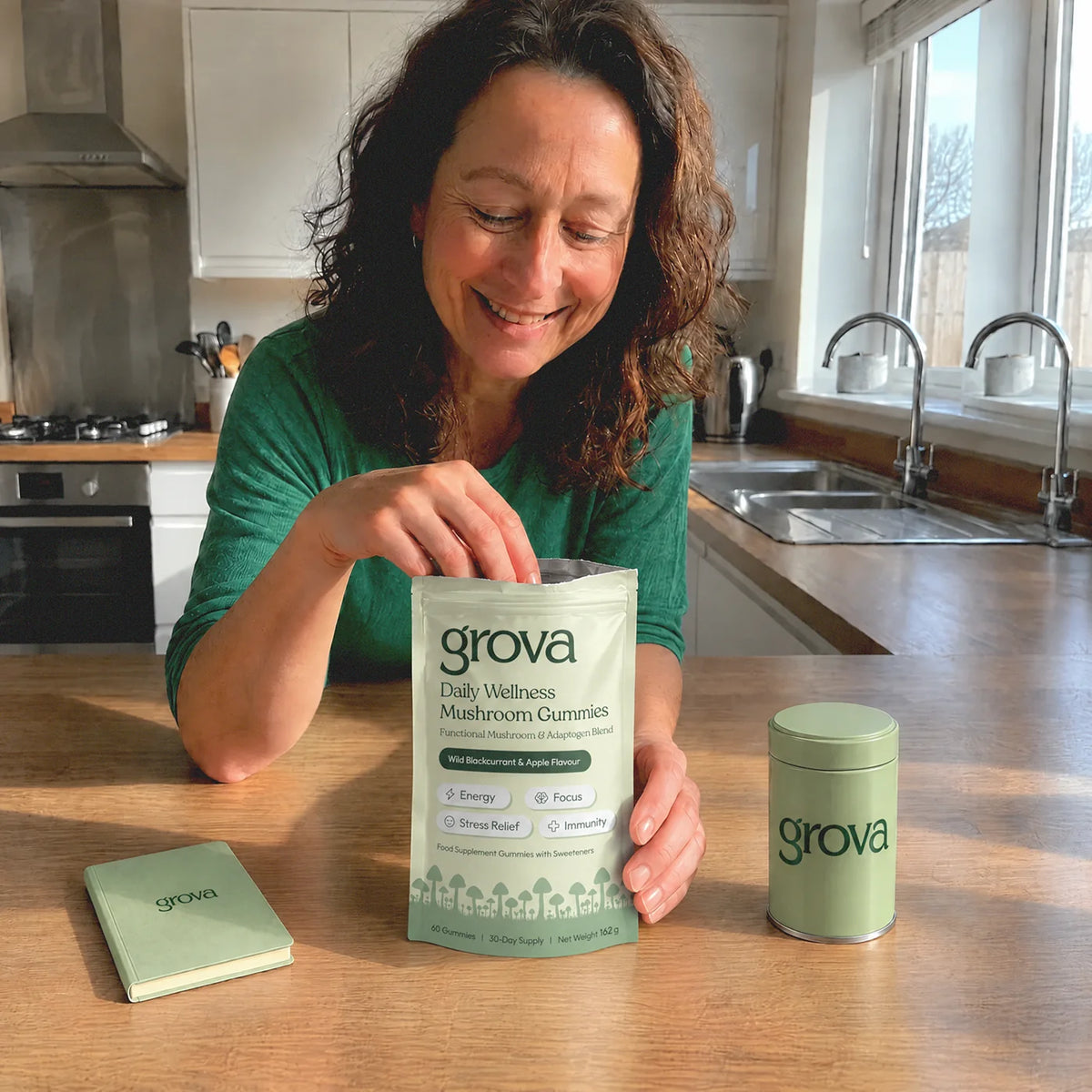 Woman reaching into a pouch of Grova Daily Wellness Mushroom Gummies beside a journal and gummy canister